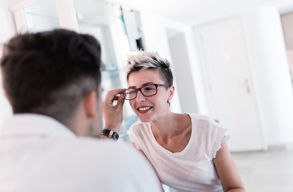 Male optometrist performing eye exam on smiling patient as she looks through eyeglasses