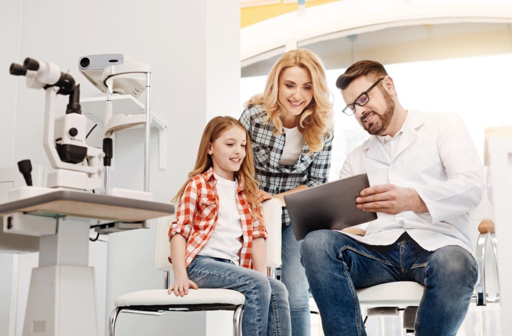 Smiling mother and daughter looking at tablet held by optometrist in office