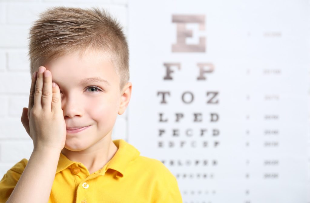 Young boy covering up right eye with eye exam chart in the background