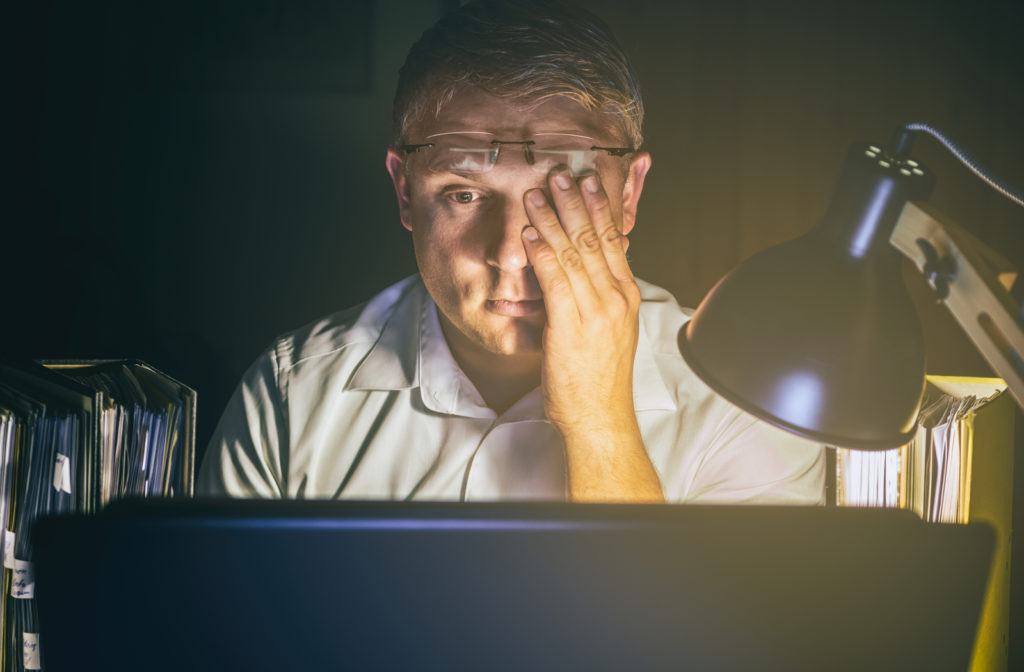 Man experiencing dry eye and touching eye with glasses on top of forehead.