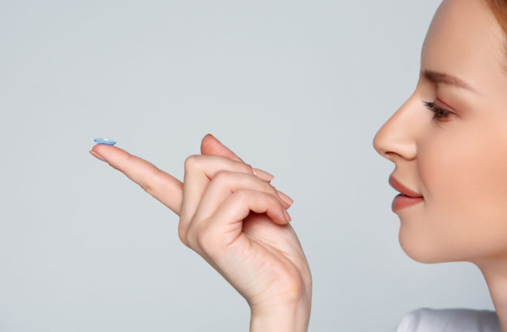 A close-up of a woman holding a contact lens at the tip of her finger doing the side view test to check if the lens is are inside out.