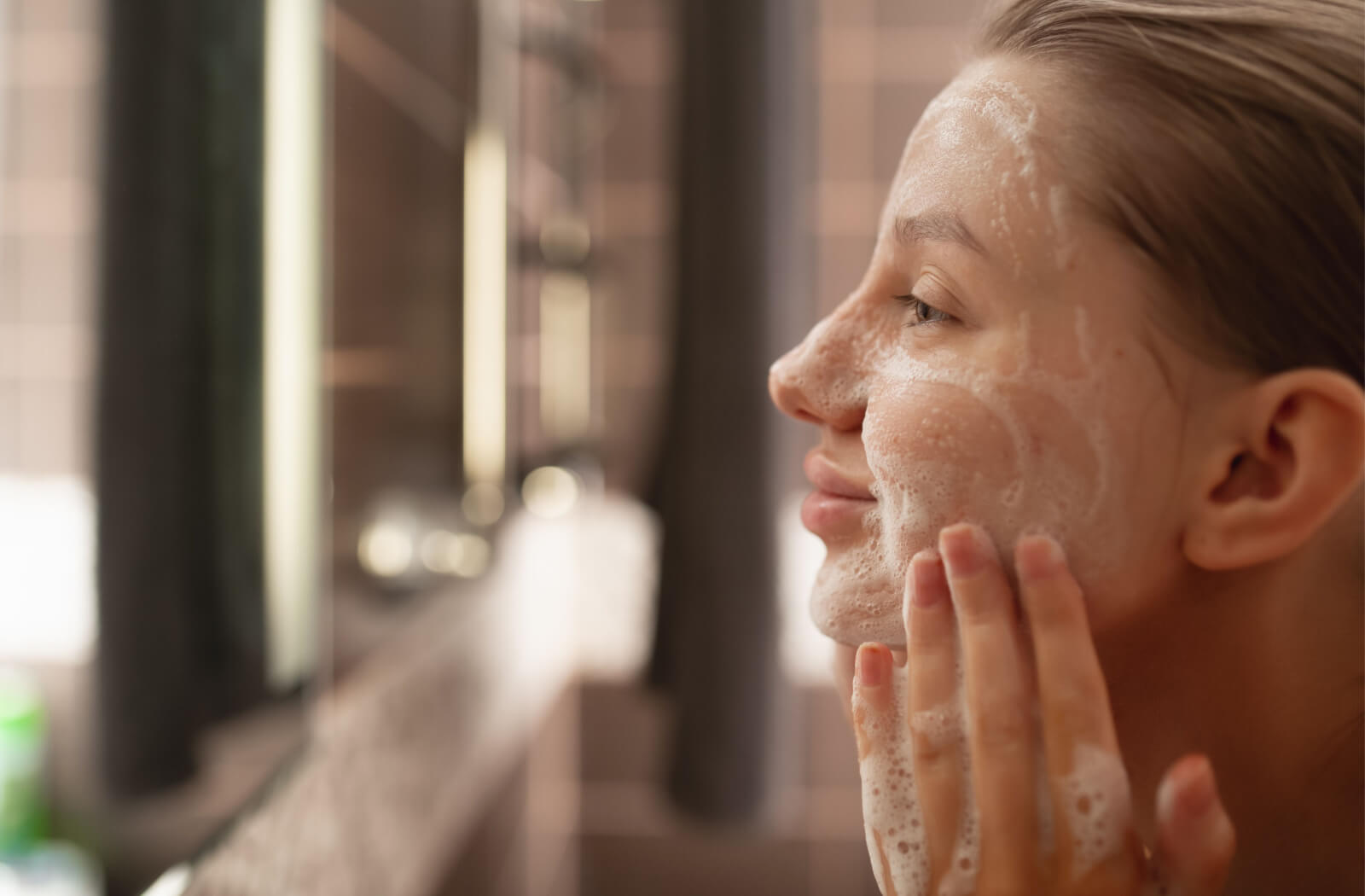 Young woman washing her face and smiling in front of a mirror.