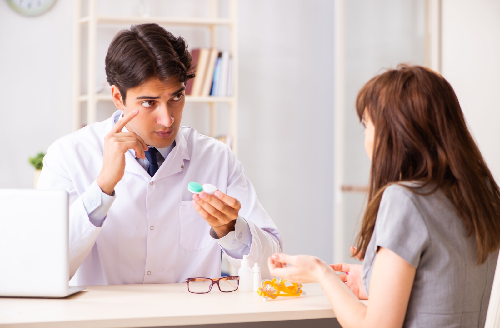 An optometrist explains proper contact lens wear and care to their patient during a contact lens fitting.