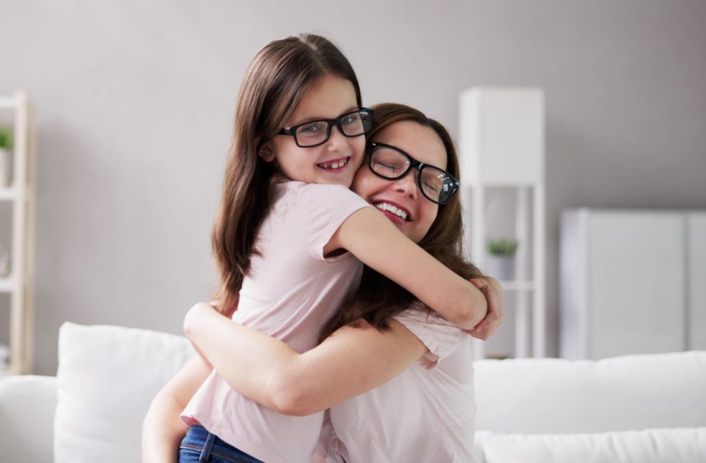 Mom and daughter hugging each other with big smiles and similar glasses.