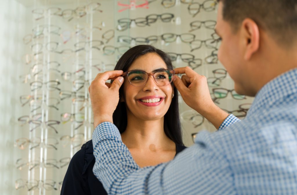 An optician fitting eyeglasses on a smiling patient.