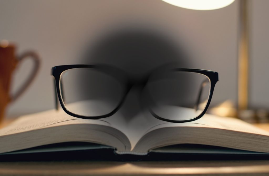 An image of eyeglasses on a book with a large dark circle in the middle of the image that demonstrates vision loss from age-related macular degeneration.