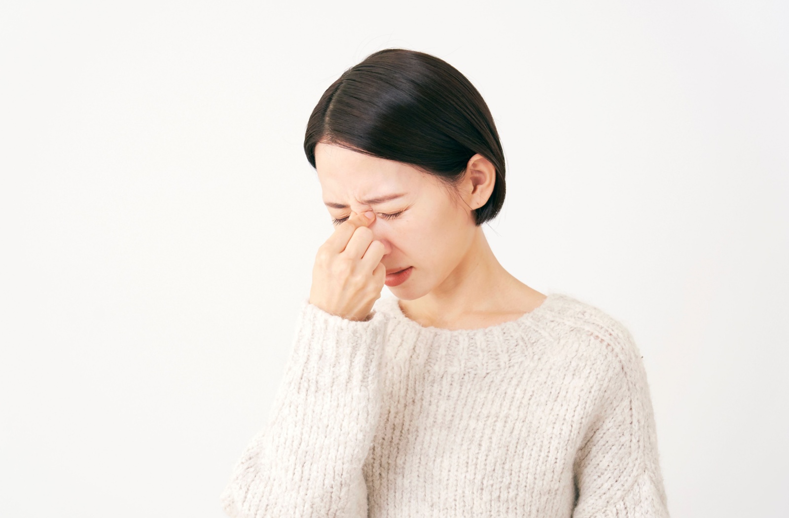 Woman rubbing her eyes, in pain, against white background.
