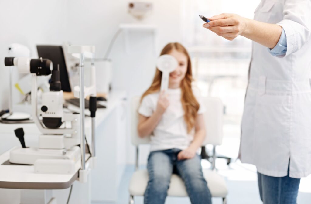 Child undergoing an eye exam holding an occluder with an optometrist conducting a visual assessment in a clinical setting