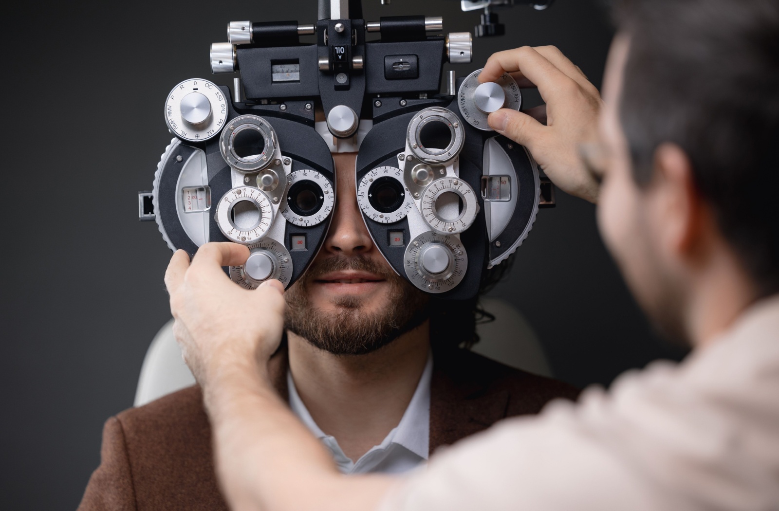 A patient sitting behind a phoropter while their optometrist adjusts the lenses.