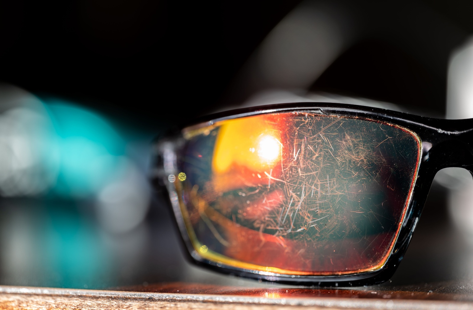 A pair of sunglasses resting on a table showing multiple scratches on its lens.