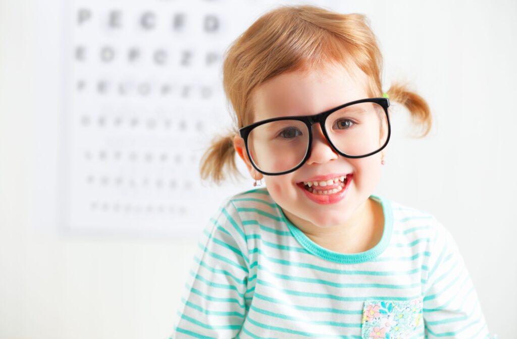 Young child wearing glasses at an eye exam with vision chart in background.