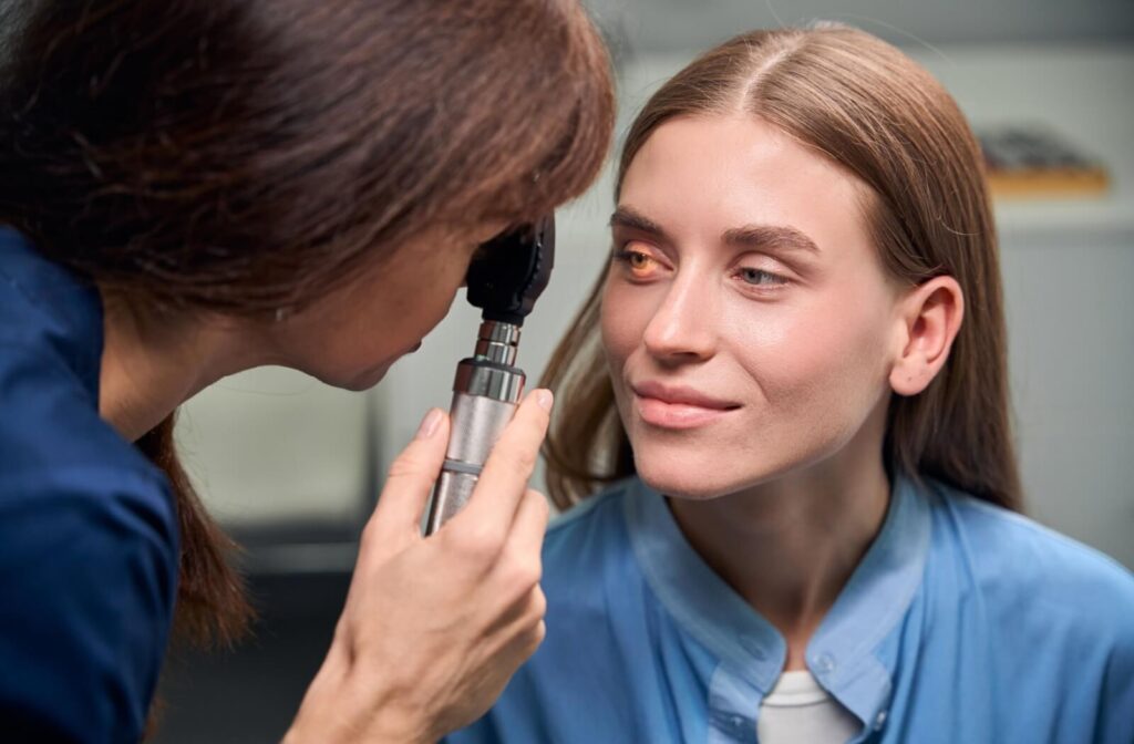 An eye care professional using a handheld ophthalmoscope to examine a patient's eye in a clinical setting.